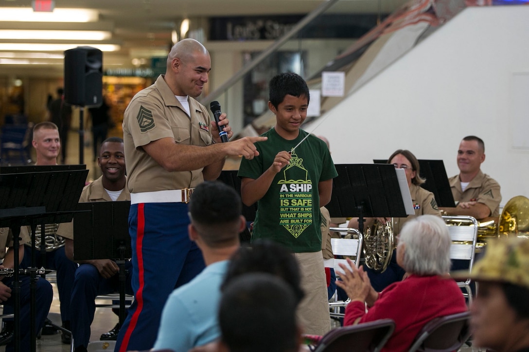 Gunnery Sgt. Francisco Gaxiola, left, teaches a young fan how to conduct a band during a patriotic concert July 19  at the Micronesia Mall in Dededo, Guam. The III Marine Expeditionary Force Band performed a list of patriotic songs in spirit of the 70th anniversary of the liberation of Guam. The band was in Guam July 18-22 to provide musical support and Marine Corps representation for liberation anniversary events. Gaxiola is a Los Angeles, California, native and the enlisted conductor with the III MEF Band.