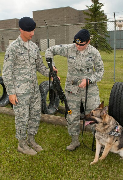 Staff Sgt. Christopher Averill, 5th Security Forces Squadron military working dog trainer, hands a practice weapon to Senior Airman Heather Johnson, 5th SFS MWD handler, during weapons training with her MWD Cyndy on Minot Air Force Base, N.D., July 29, 2014. Averill adheres to a master training plan that outlines the requirements for new handlers. He also works side by side with the handlers to demonstrate proper techniques and methods for working with their MWD. (U.S. Air Force photo/Senior Airman Stephanie Morris)