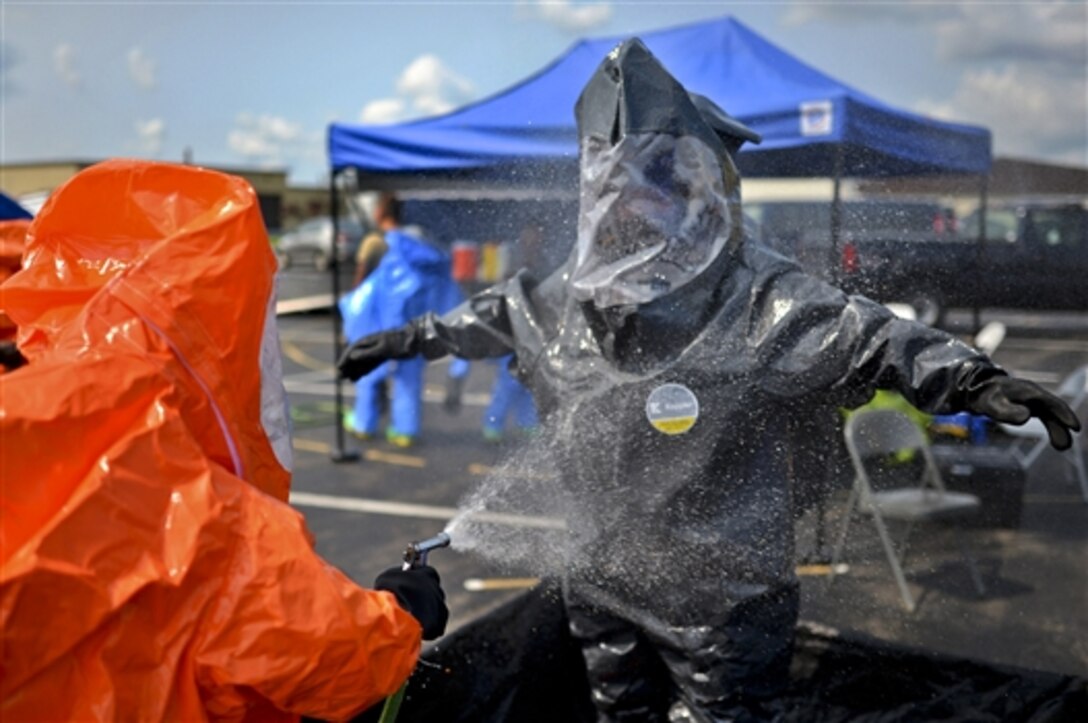 An airman uses a hose to spray off another airman's protective clothing while conducting a hazardous environment drill on Niagara Falls Air Reserve Base in Niagara Falls, N.Y., Aug. 9, 2014. The airmen are assigned to the New York Air National Guard. After completing the course, the airmen will be certified to chemically decontaminate an area and provide first-line medical care to civilian victims.