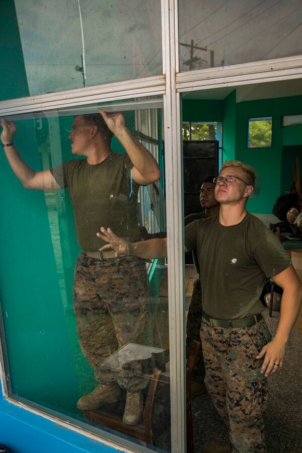 U.S. Marines from 8th Engineer Support Battalion, 2nd Marine Logistics Group, reinstall a piece of glass in order to reapply a water proofing seal around the edges of the window pane. The Guatemala Brigada de Infanteria de Marina (BIM) engineers along with their U.S. counterparts help renovate the Biblioteca Municipal Corporacion 74-78 as part of a humanitarian engineering project in Puerto Barrios, Guatemala, Aug. 14, 2014. The Marines and Sailors are helping to remodel buildings in support of Southern Partnership Station 2014, a combined joint exercise focused on subject matter expert exchanges with partner nations and security forces as well as military to military engagements and community relations projects in Central America. (U.S.  Marine Corps photo by Lance Cpl. Chloe Nelson, 2D MAR DIV Combat Camera/ Released)