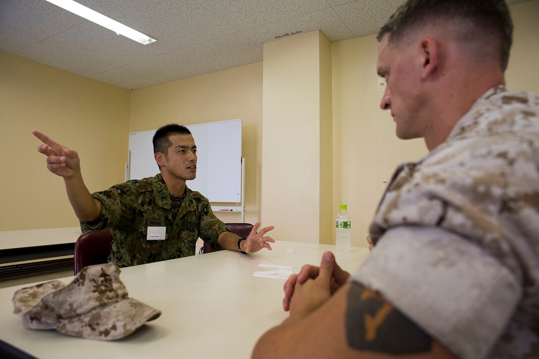 Master Sgt. Hideyuki Watabe, an infantryman with the Japanese Ground Self-Defense Force’s 13th Brigade, 46th Regiment, left, explains aspects of JGSDF training to Sgt. Giancarlo Maragni, a Corporals Couse instructor from Marine Corps Air Station Iwakuni, Japan, during an English seminar aboard JGSDF Base Kaita in Hiroshima, August 8, 2014. The purpose behind the tour was to provide Marines the opportunity to visit and experience the Japanese military lifestyle and training requisites.