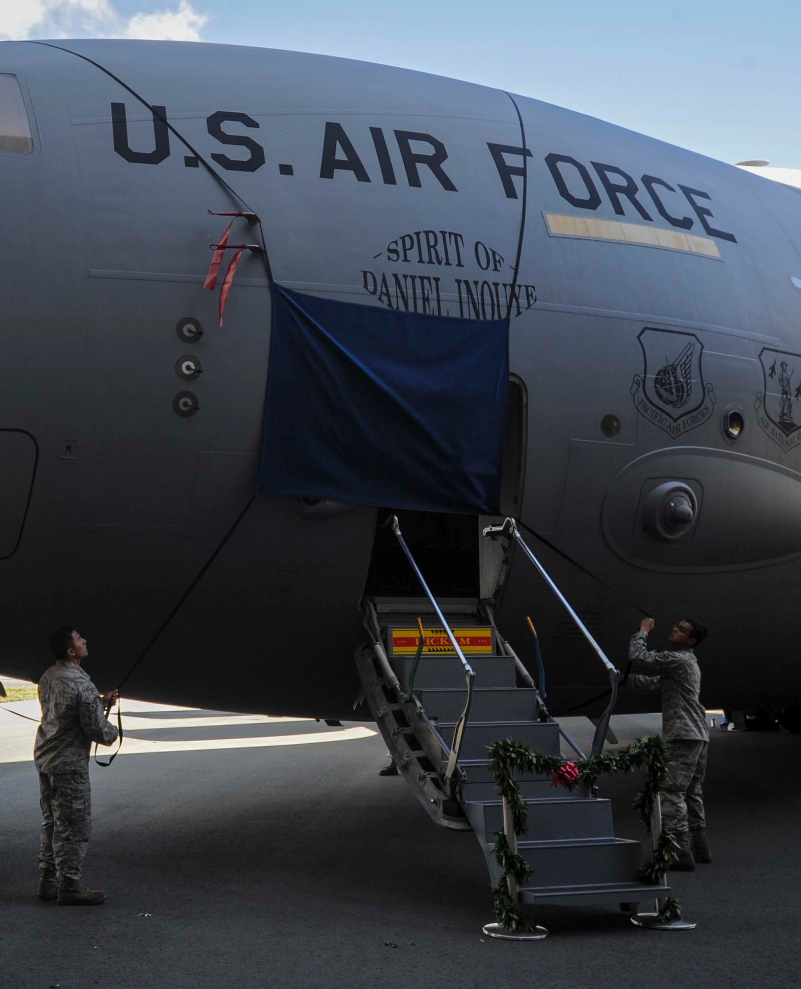 Tech. Sgt. Dustin Ching, 154th Aircraft Maintenance Squadron crew chief, left, and Staff Sgt. Steven Devenecia, 15th Aircraft Maintenance Squadron crew chief, right, unveil the artwork for the newly dedicated “Spirit of Daniel Inouye” C-17 Globemaster III following the ceremony on the Joint Base Pearl Harbor-Hickam, Hawaii, flightline Aug. 20, 2014. During the ceremony, the 535th Airlift Squadron cargo aircraft was dedicated to the memory of local and national hero and Medal of Honor recipient Sen. Daniel Inouye. (U.S. Air Force photo by Tech. Sgt. Terri Paden)