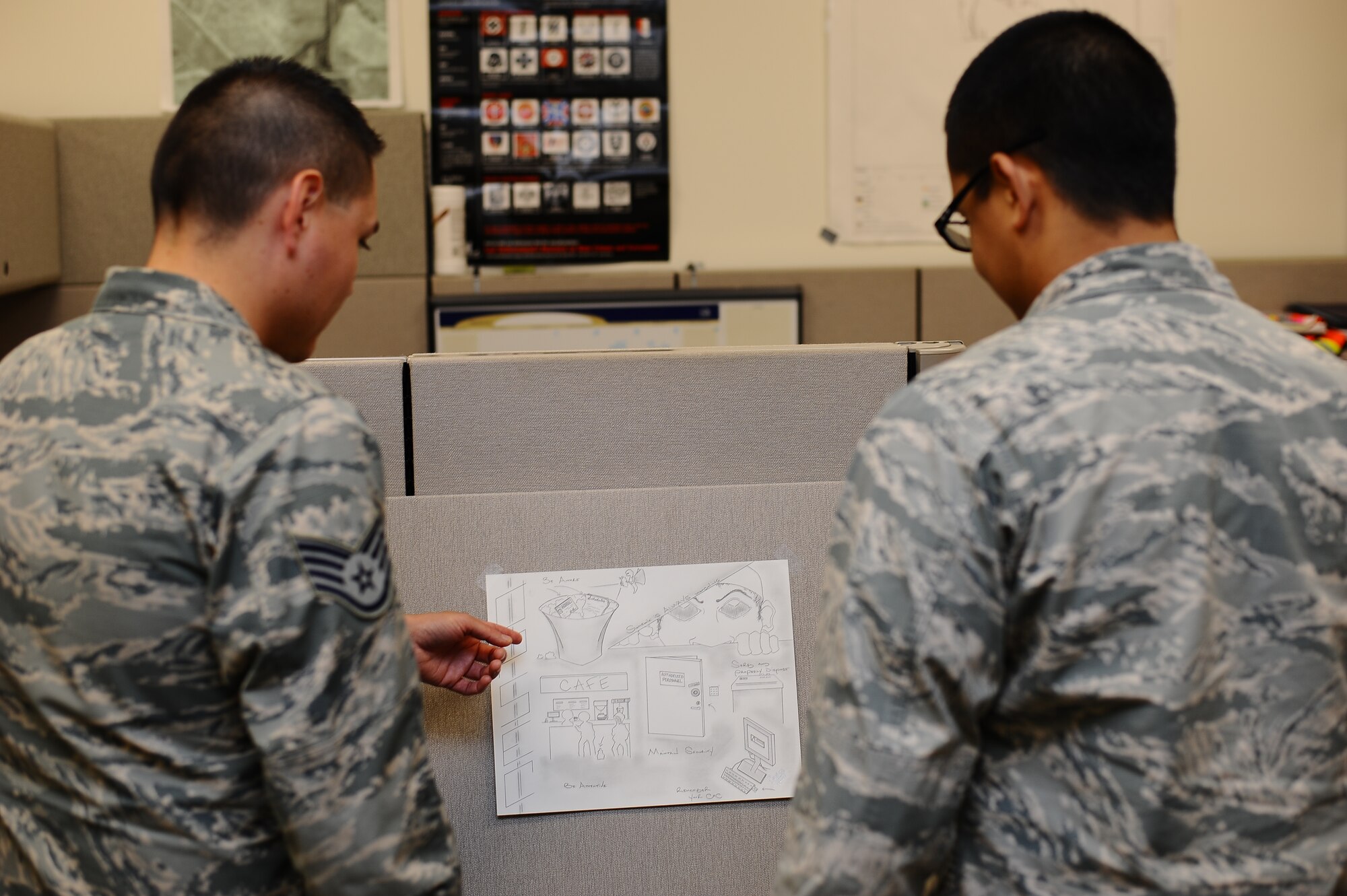 Airmen from the 460th Space Wing Plans and Programs office view the winning poster from the Operations Security poster contest on Buckley. The poster, submitted by Staff Sgt. Ashley Glasgow, 460th Security Forces Squadron supervisor, will go on to compete with other posters at Air Force Space Command. (U.S. Air Force photo by Senior Airman Darren Scott/Released)