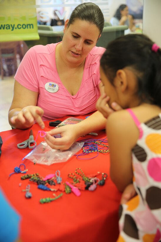 Alexis Rose, left, demonstrates how to make a backpack key chain for a participant at Marine Corps Air Station Cherry Point's back-to-school event Aug. 14, 2014. Craft stations were set up for children to make a zipper-pull key chain for their backpack and fill out a time capsule sheet to reopen at the end of the year for the children to see how their lives have changed. During the event, children of active-duty and reserve service members met with Disney Channel star Sabrina Carpenter for photos and autographs. The event ended with the back-to-school fashion show, where a parade of active-duty service member's children modeled clothing and accessories available for purchase at the exchange. Rose is the information and referral specialist with Marine Corps Community Services Personal and Professional Development. 
