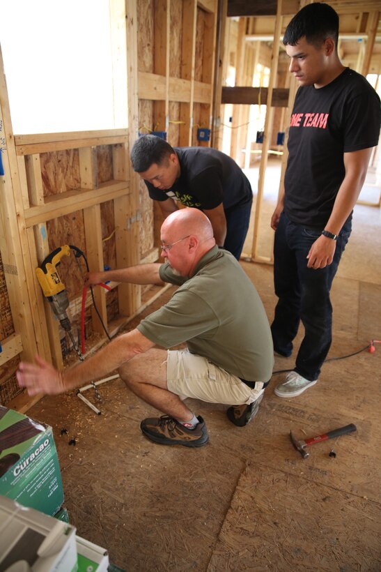 Michael Dorman, center, demonstrates to two volunteers the proper way to use a drill to run wires in a home during a construction project Aug. 17, 2014, during the Military Missions in Action American Heroes Home Build of Pamlico County.  Dorman is the executive director of Military Missions in Action.