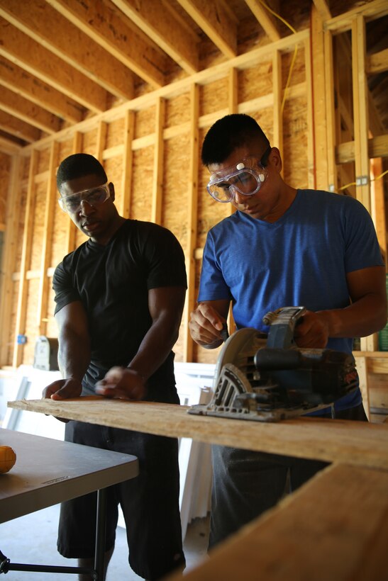 Lance Cpl Tristan Ebanks, left, and Pfc. Angel Ortiz use a saw to cut a piece of wood during a construction project Aug. 17, 2014, for the Military Missions in Action American Heroes Home Build of Pamlico County.  Ebanks is an aircraft electronic countermeasures systems technician and Ortiz is an aviation ordnance technician with the Center for Naval Aviation and Technical Training at Marine Corps Air Station Cherry Point.