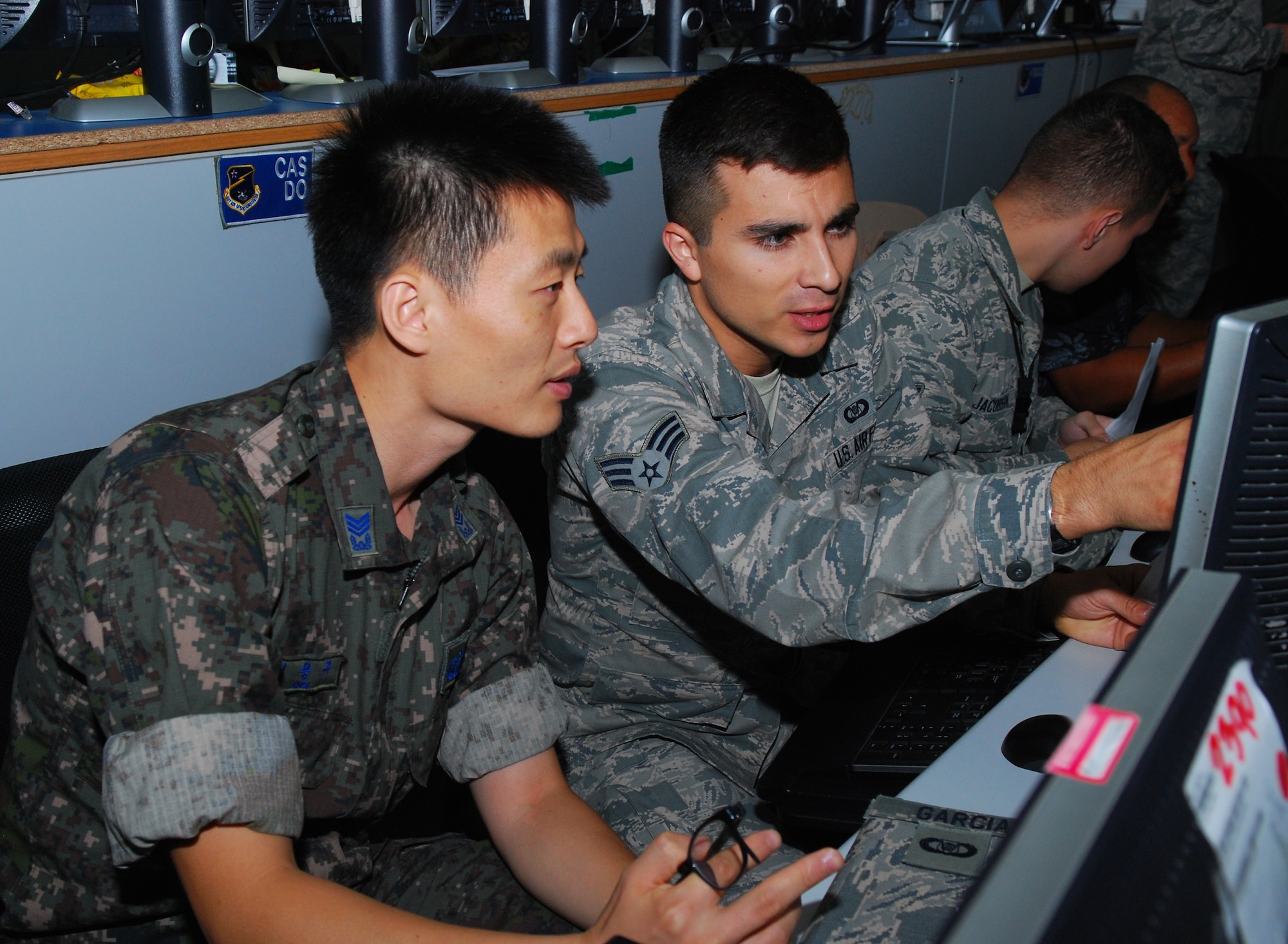Senior Airman Jose Garcia, 701st Combat Operations Squadron command control battle management operator, discusses operations with Master Sgt. Young Kyo Choi, Republic of Korea Air Force command control battle management counterpart, at the Harden Theater Air Control Center, Osan Air Base, South Korea, during Ulchi Freedom Guardian, Aug. 20, 2014. UFG tests and builds the U.S.-ROK alliance commanders’ and staff members’ ability to translate information into actionable decision-making. (U.S. Air Force photo by Senior Airman Racheal E. Watson/Released)