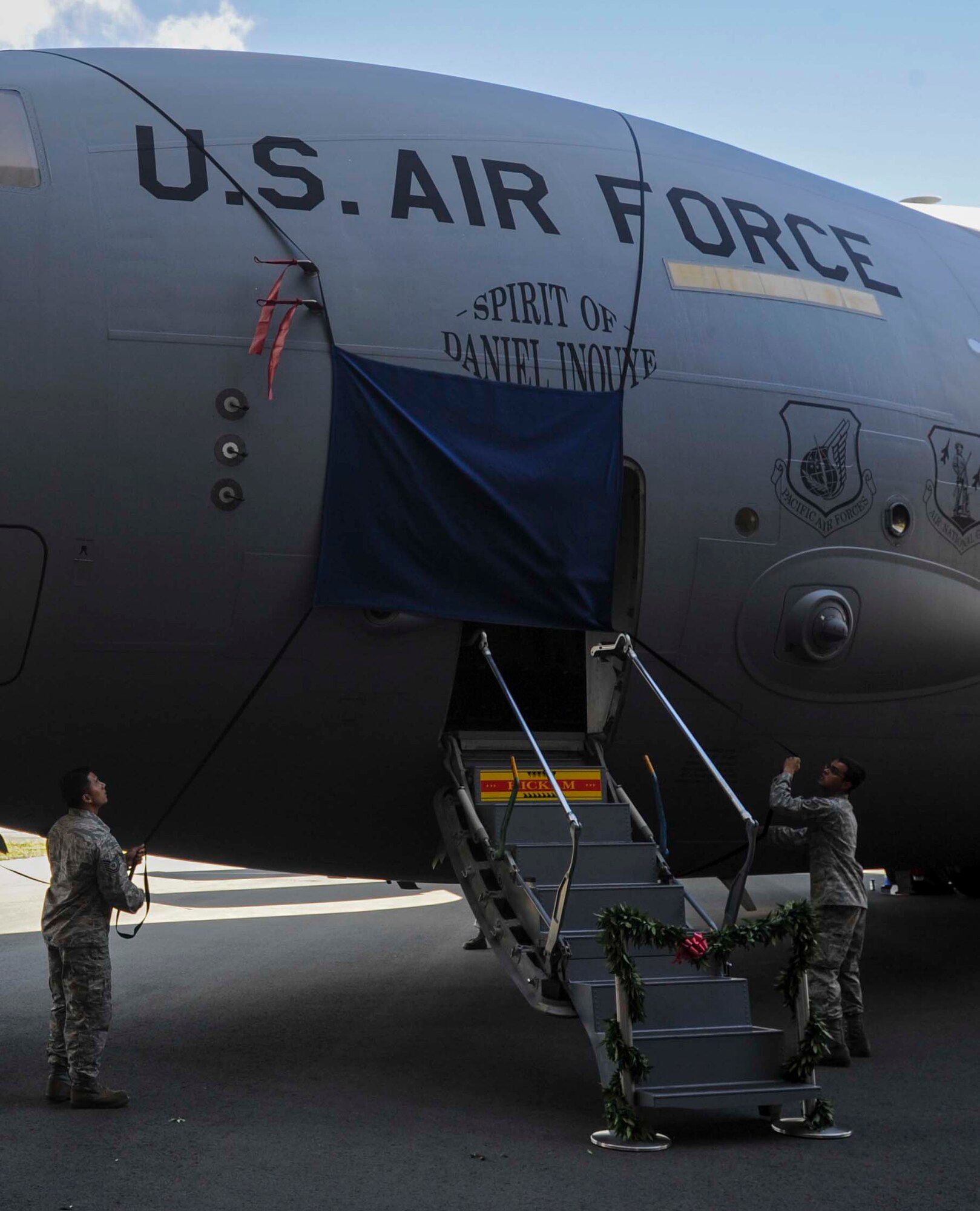 Tech. Sgt. Dustin Ching, left, and Staff Sgt. Steven Devenecia unveil the artwork for the newly dedicated “Spirit of Daniel Inouye” C-17 Globemaster III Aug. 20, 2014, following a ceremony on the flightline at Joint Base Pearl Harbor-Hickam, Hawaii. During the ceremony, the 535th Airlift Squadron cargo aircraft was dedicated to the memory of local and national hero, and Medal of Honor recipient Sen. Daniel Inouye. Ching is a 154th Aircraft Maintenance Squadron crew chief and Devenecia is a 15th Aircraft Maintenance Squadron crew chief. (U.S. Air Force photo/Tech. Sgt. Terri Paden)