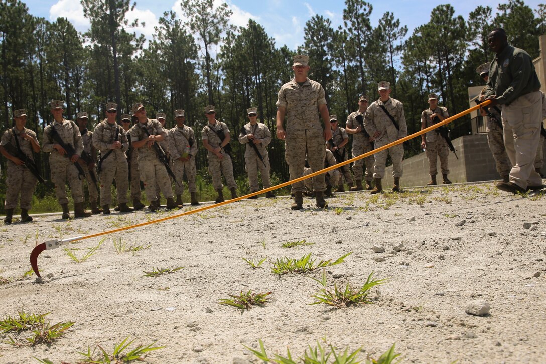 Marines from Combat Logistics Battalion 2, 2nd Marine Logistics Group, pay close attention as counter-IED instructor and retired Marine Corps Master Sgt. David Slay demonstrates how to use a holley stick to find loose wires, bombs, or battery packs underground August 19, 2014 in Holly Ridge, North Carolina.  The holley stick, comprised of a 15-foot pole with a sicle head attached, was named after it's inventor, Explosive Ordinance Technician Gunnery Sgt. Floyd C. Holley.  "To date, no Marines have been killed using the holley stick," said counter-IED instructor Travis Hiller.