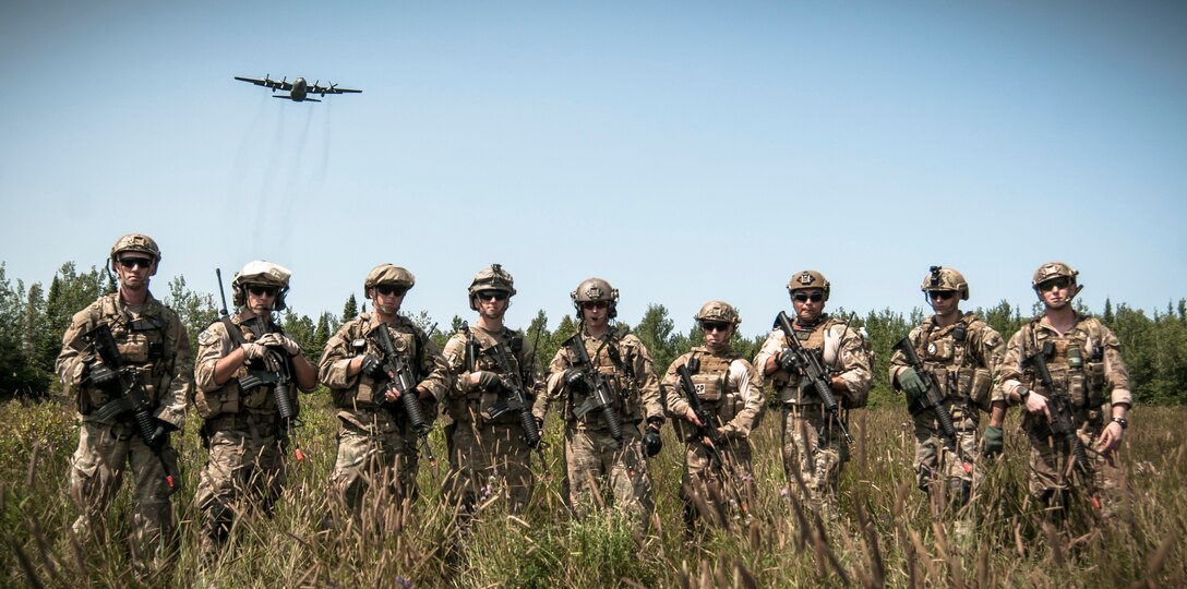 Joint tactical air controllers from the 169th Air Support Operations Squadron, Peoria, Ill., pose for a photo while a C-130 Hercules from the 182nd Airlift Wing, Peoria, Ill., flies overhead during Operation Northern Strike 2014 near Rogers City, Mich., on Aug. 6, 2014. Operation Northern Strike 2014 is a joint multi-national combined arms training exercise conducted in Michigan. (U.S. Air National Guard photo by Master Sgt. Scott Thompson/released)
