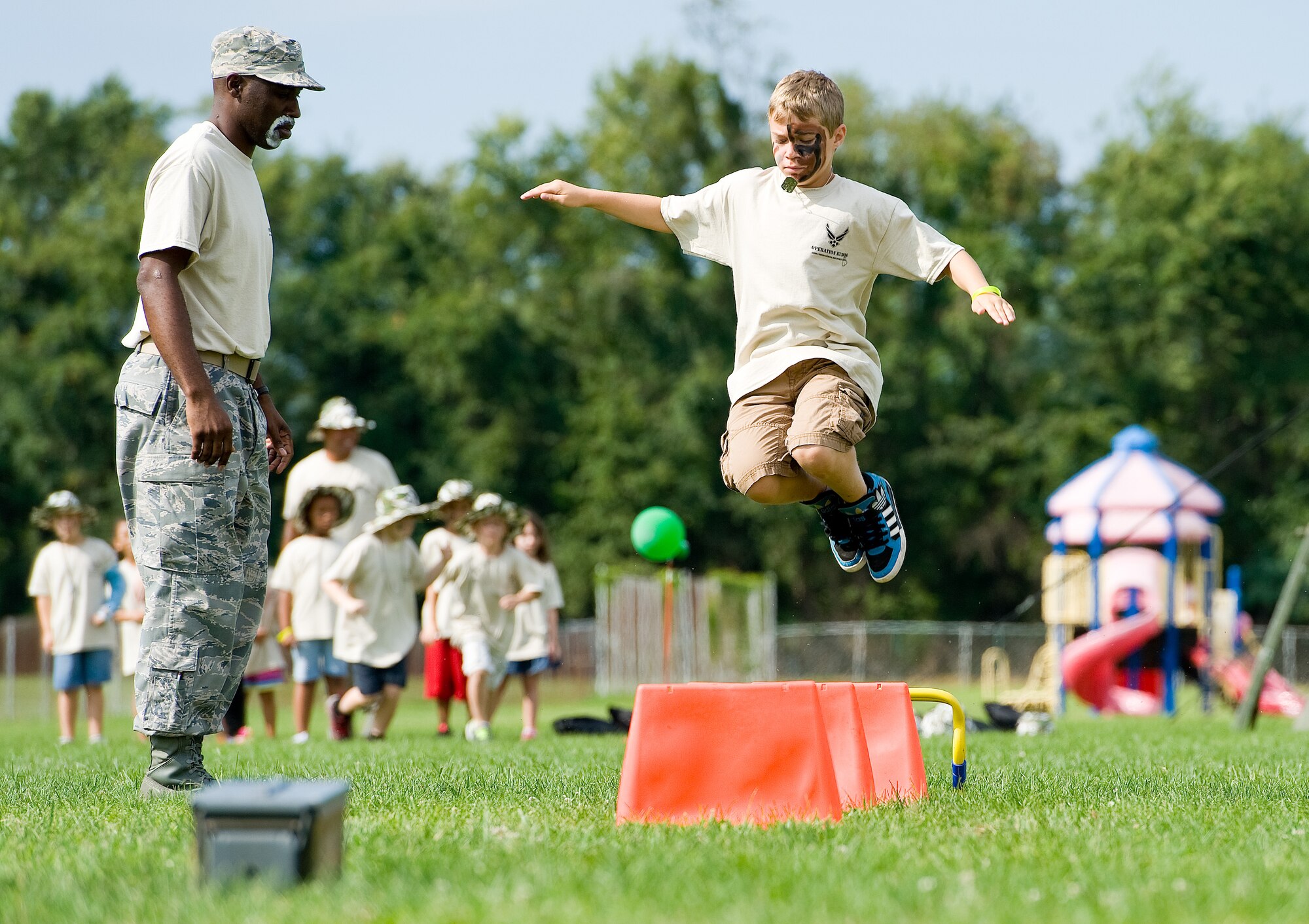 Tech. Sgt. Shon Steed, Air Force Mortuary Affairs Operations, watches Aiden Weil, son of Tech. Sgt. Jeannie Medeiros, 736th Aircraft Maintenance Squadron, jump over obstacles Aug. 20, 2014, at the Youth Center on Dover Air Force Base, Del. The Youth Center hosted KUDOS, Kids Understanding Deployment Operations that allowed children the opportunity to process through a simulated deployment processing line and engage a few obstacle courses. (U.S. Air Force photo/Roland Balik)