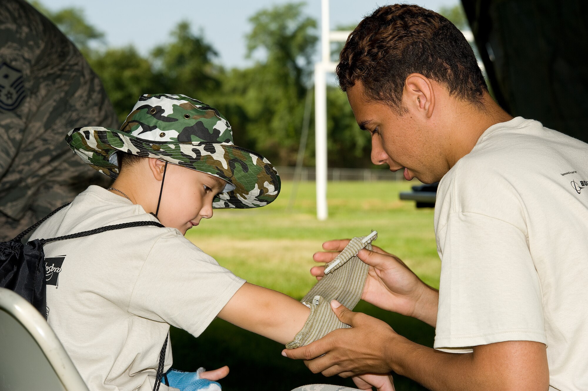 Senior Airman Dominique Washington, 436th Dental Squadron, wraps a bandage around the arm of Anthony Bonanno, son of Stephanie Montes, Joint Personal Effects Depot, Aug. 20, 2014, at the Youth Center on Dover Air Force Base, Del. Bonanno was one of 161 children that processed through the KUDOS, Kids Understanding Deployment Operations simulated deployment line. (U.S. Air Force photo/Roland Balik)
