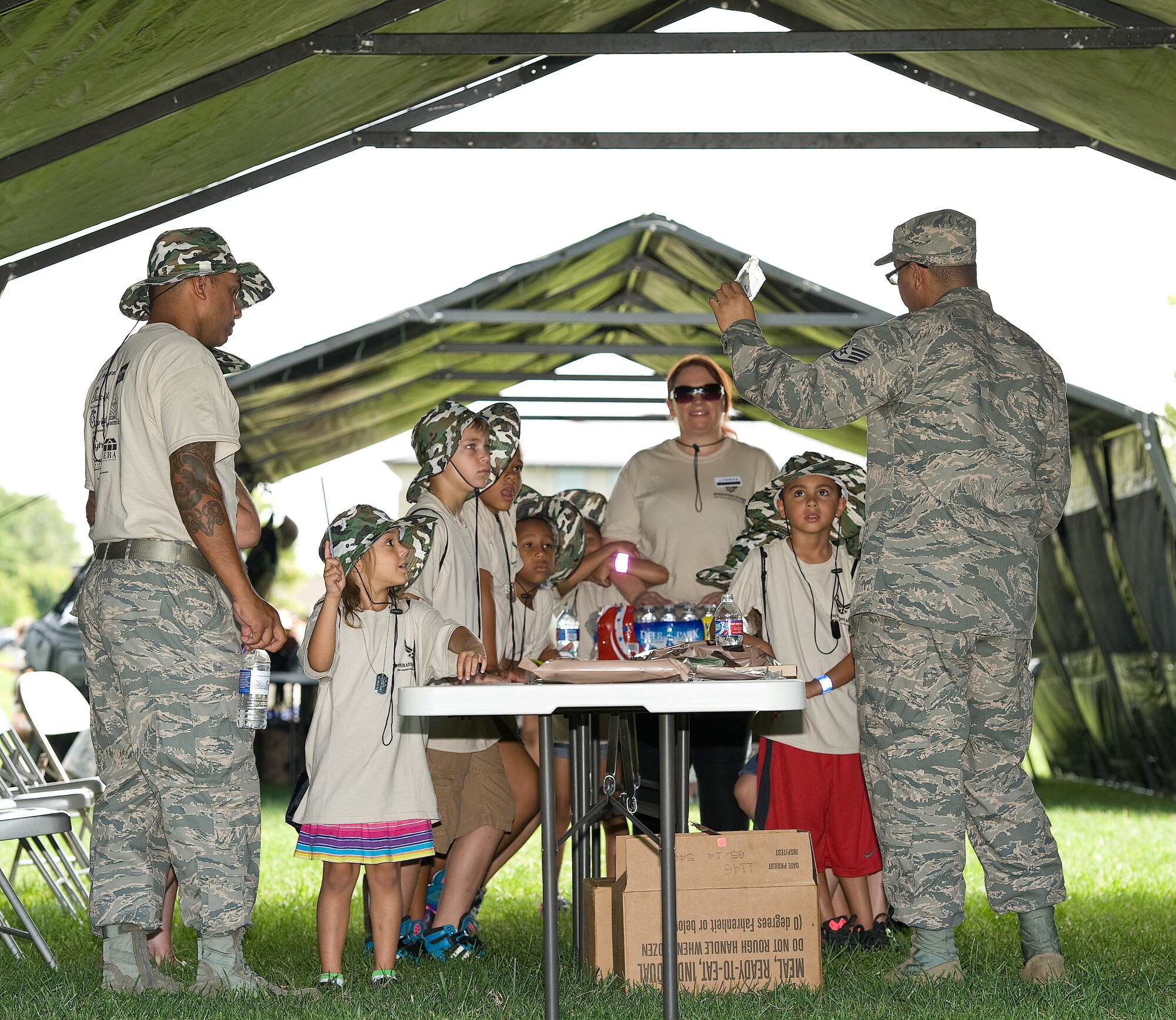Master Sgt. Ruben Mojica, left, and Staff Sgt. Brian Sosa, both with the 436th Force Support Squadron, display items to children going through the meals, ready to eat tent Aug. 20, 2014, at the Youth Center on Dover Air Force Base, Del. KUDOS, Kids Understanding Deployment Operations allowed children to go through a simulated deployment processing line and numerous obstacle courses. (U.S. Air Force photo/Roland Balik)