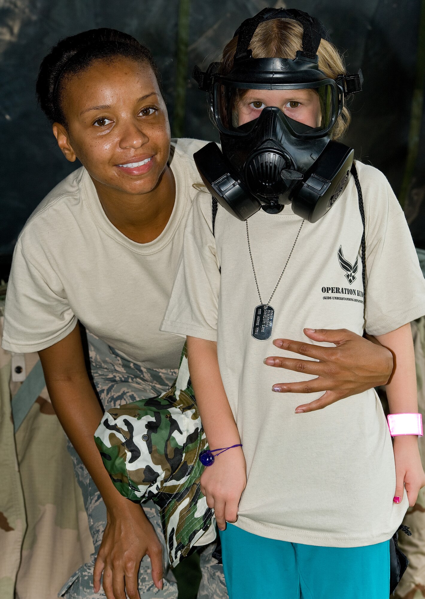 Tech. Sgt. Zizanie Deravin, 436th Logistics Readiness Squadron, left, poses for a photo with Morgan Funk, daughter of Master Sgt. Gregory and Christina Funk, 512th Aerospace Medicine Squadron, after donning a chemical mask Aug. 20, 2014, at the Youth Center on Dover Air Force Base, Del. One hundred sixty-one children processed through the simulated deployment line during the KUDOS, Kids Understanding Deployment Operations event. (U.S. Air Force photo/Roland Balik)
