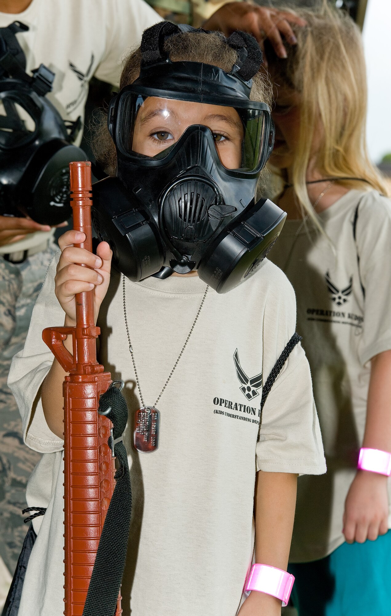 Isabella Richmond, daughter of Master Sgt. Amy Perez, 436th Civil Engineer Squadron, wears a chemical mask while holding onto a simulated M-16 training weapon Aug. 20, 2014, at the Youth Center on Dover Air Force Base, Del. Children signed up for KUDOS, Kids Understanding Deployment Operations through the Youth Center. The event allowed them to experience going through a deployment line tailored for children. (U.S. Air Force photo/Roland Balik)