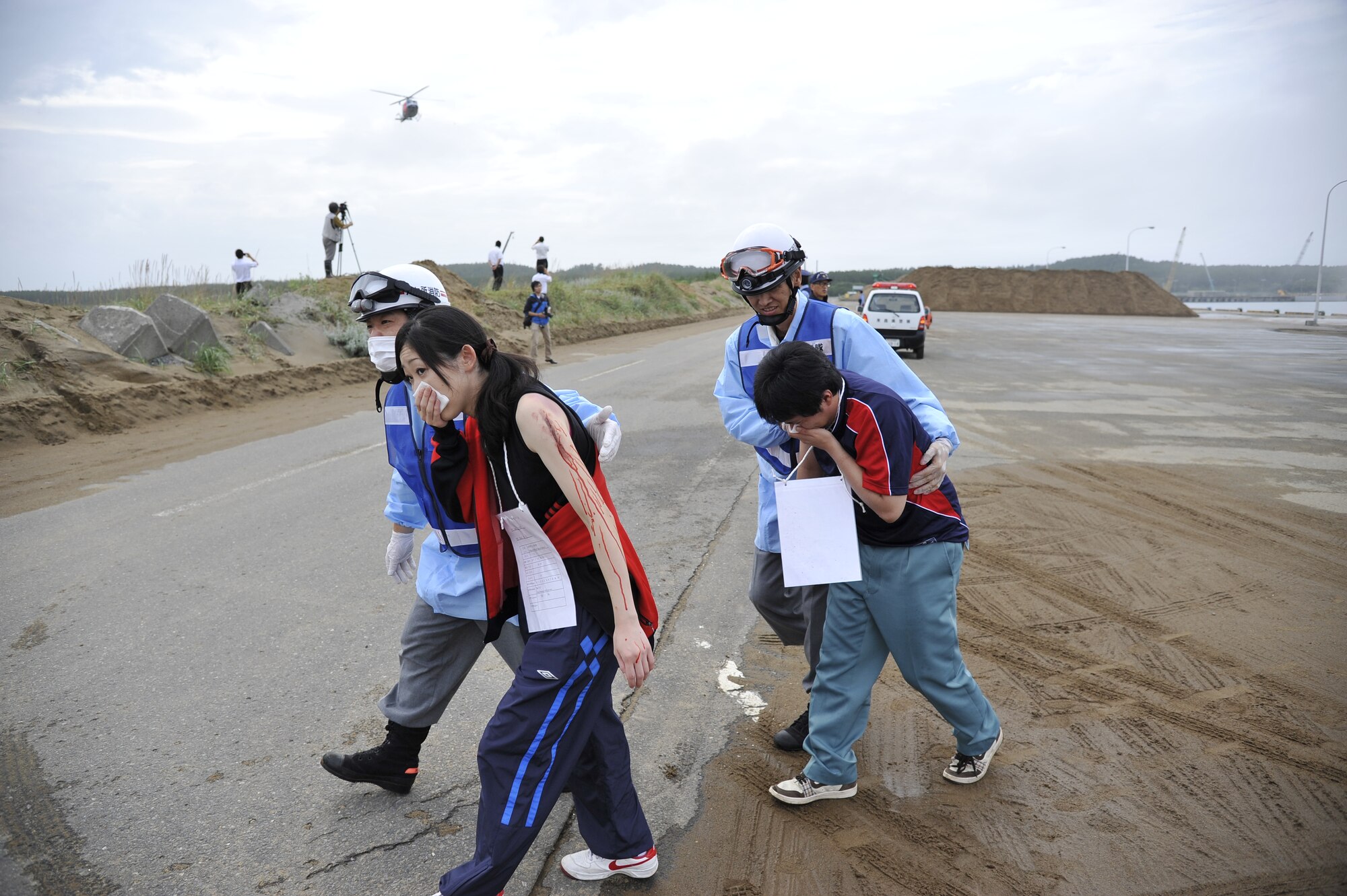 Two members from the Rokkasho Village fire department escort two simulated injured civilians from the site of an accident during a Major Accident Response Exercise at Rokkasho Village, Japan, Aug. 19, 2014. The scenario involved an F-16 Fighting Falcon "crash landing" in Rokkasho Village, resulting in 11 civilian injuries which required immediate care from responding agencies. (U.S. Air Force photo by Airman 1st Class Patrick S. Ciccarone/Released)