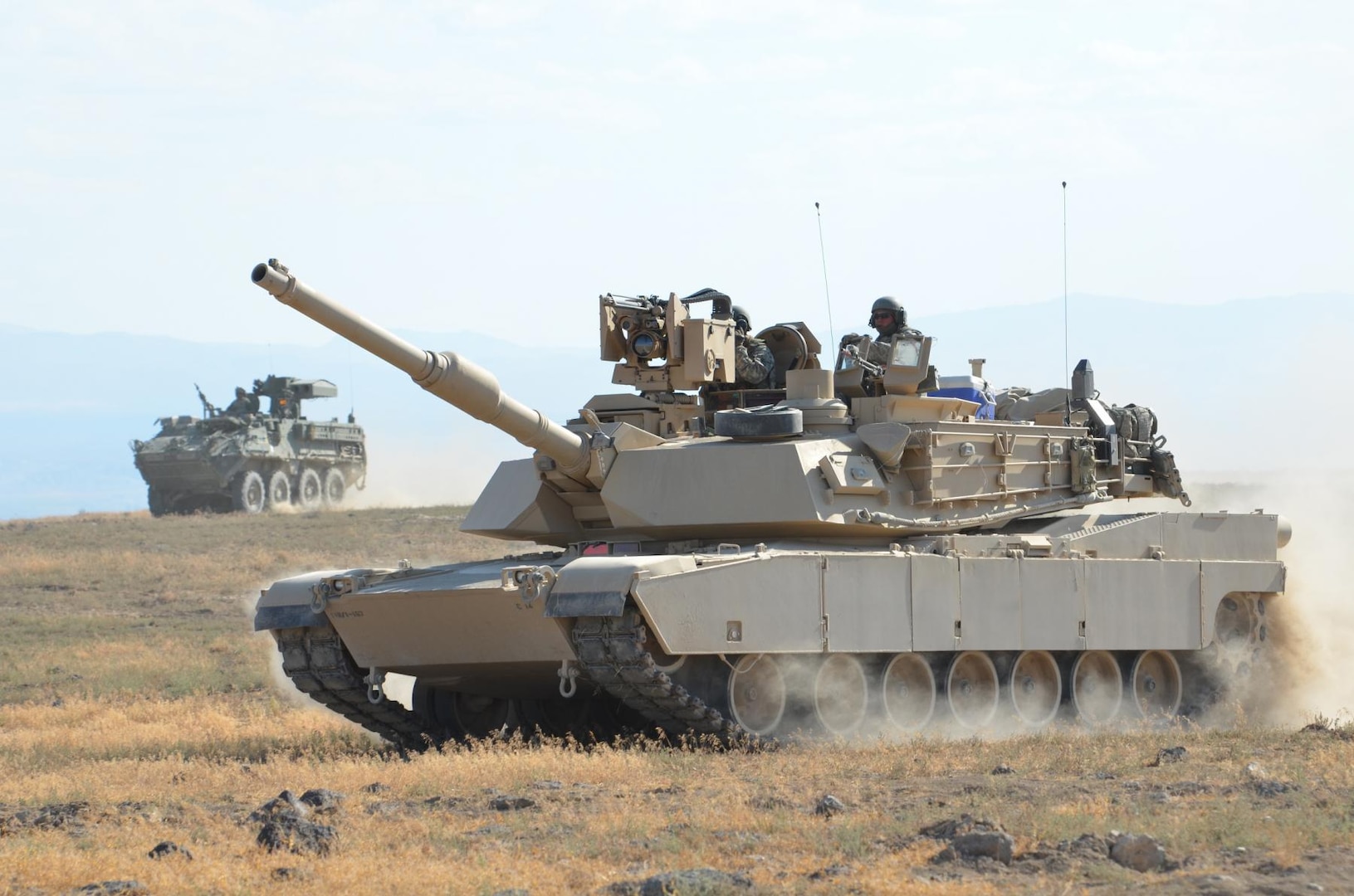 An M1A2 SEP Abrams from 116th Cavalry Brigade Combat Team, Idaho Army National Guard (middle) and a M1134 Anti-Tank Guided Missile Vehicle from 1st Squadron, 14th Infantry Regiment, 3rd Stryker Brigade Combat Team, Joint Base Lewis-McChord, Washington, return from waging mock battle against one another during an eXportable Combat Training Capability exercise, at Orchard Combat Training Center, south of Boise, Idaho, Aug. 14, 2014.