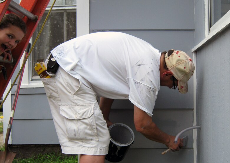 John Bertino, Engineering Division Chief at Omaha District does some last minute paint touch ups during the 2014 Paint-A-Thon, while his daughter Jill peeks through the steps of one of the many ladders used during the painting of the home in Council Bluffs, Iowa.