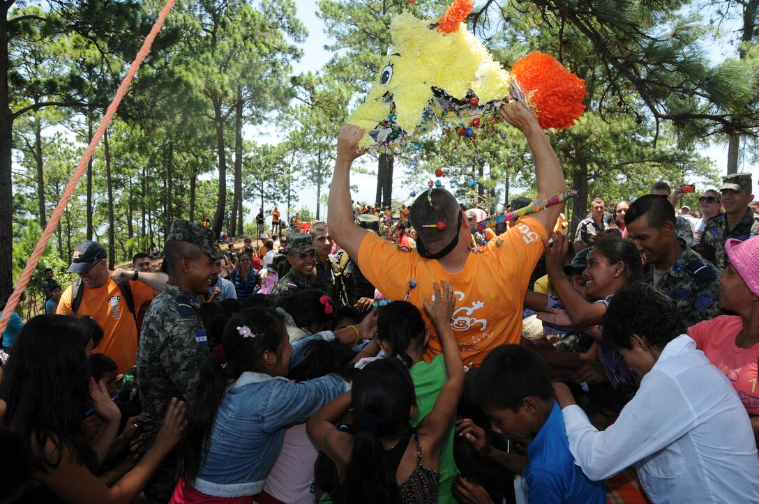 Children swarm to gather candy as U.S. Air Force Capt. Jeffrey Scott tears open a piñata. Over 130 members of Joint Task Force-Bravo, with the support of Joint Task Force-Bravo’s Joint Security Forces and Honduran Air Force cadets, hiked nearly eight miles round trip to deliver more than 2,700 pounds of food and supplies to families in need in the mountain village of Soso Mico outside La Paz, Honduras, Aug. 23, 2014.  The effort was part of the 56th Joint Task Force-Bravo Chapel Hike, a venerable tradition during which service members donate their money and time to purchase food and supplies and then tote them on a hike through the mountains to deliver to local, underserviced communities.  (Photo by U.S. Air National Guard Capt. Steven Stubbs)