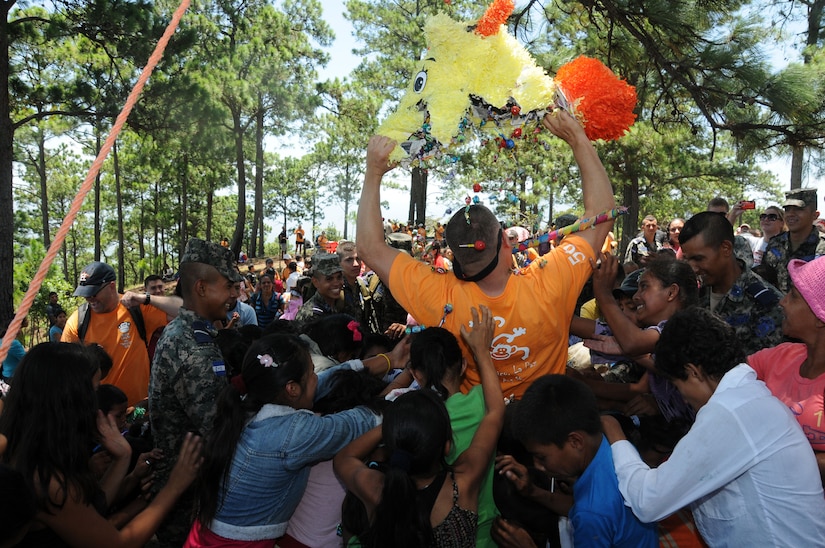 Children swarm to gather candy as U.S. Air Force Capt. Jeffrey Scott tears open a piñata. Over 130 members of Joint Task Force-Bravo, with the support of Joint Task Force-Bravo’s Joint Security Forces and Honduran Air Force cadets, hiked nearly eight miles round trip to deliver more than 2,700 pounds of food and supplies to families in need in the mountain village of Soso Mico outside La Paz, Honduras, Aug. 23, 2014.  The effort was part of the 56th Joint Task Force-Bravo Chapel Hike, a venerable tradition during which service members donate their money and time to purchase food and supplies and then tote them on a hike through the mountains to deliver to local, underserviced communities.  (Photo by U.S. Air National Guard Capt. Steven Stubbs)