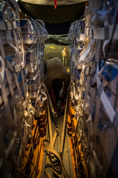 U.S. Air Force Staff Sgt. Dave Henson, 737th Expeditionary Airlift Squadron loadmaster, secures a cargo strap holding water bundles aboard a C-130H Hercules Aug. 9, 2014, before a humanitarian airdrop over Iraq. The 737th EAS aircrew dropped 1,522 gallons of bottled water for displaced citizens near Sinjar, Iraq. (U.S. Air Force photo by Staff Sgt. Jeremy Bowcock)