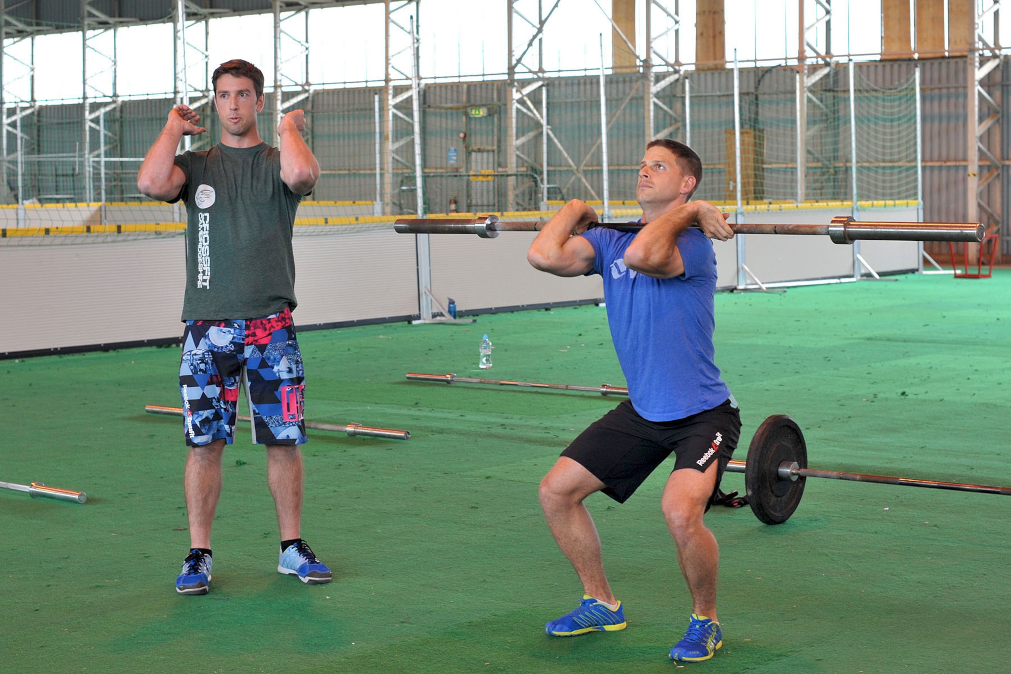 Mike Healey, left, National Geospatial Intelligence Agency intelligence analyst from Waterford, Maine, describes the proper way to perform a thruster as U.S. Army Capt. Barclay Keay, U.S. Africa Command operations branch chief, demonstrates the procedure before the start of the Coe Hero workout of the day at RAF Molesworth, United Kingdom, Aug. 14, 2014. Hero WODs are an intense workout to honor U.S. military, civilians, police officers and firefighters who have sacrificed their lives while on duty. (U.S. Air Force photo by Staff Sgt. Ashley Hawkins/Released)