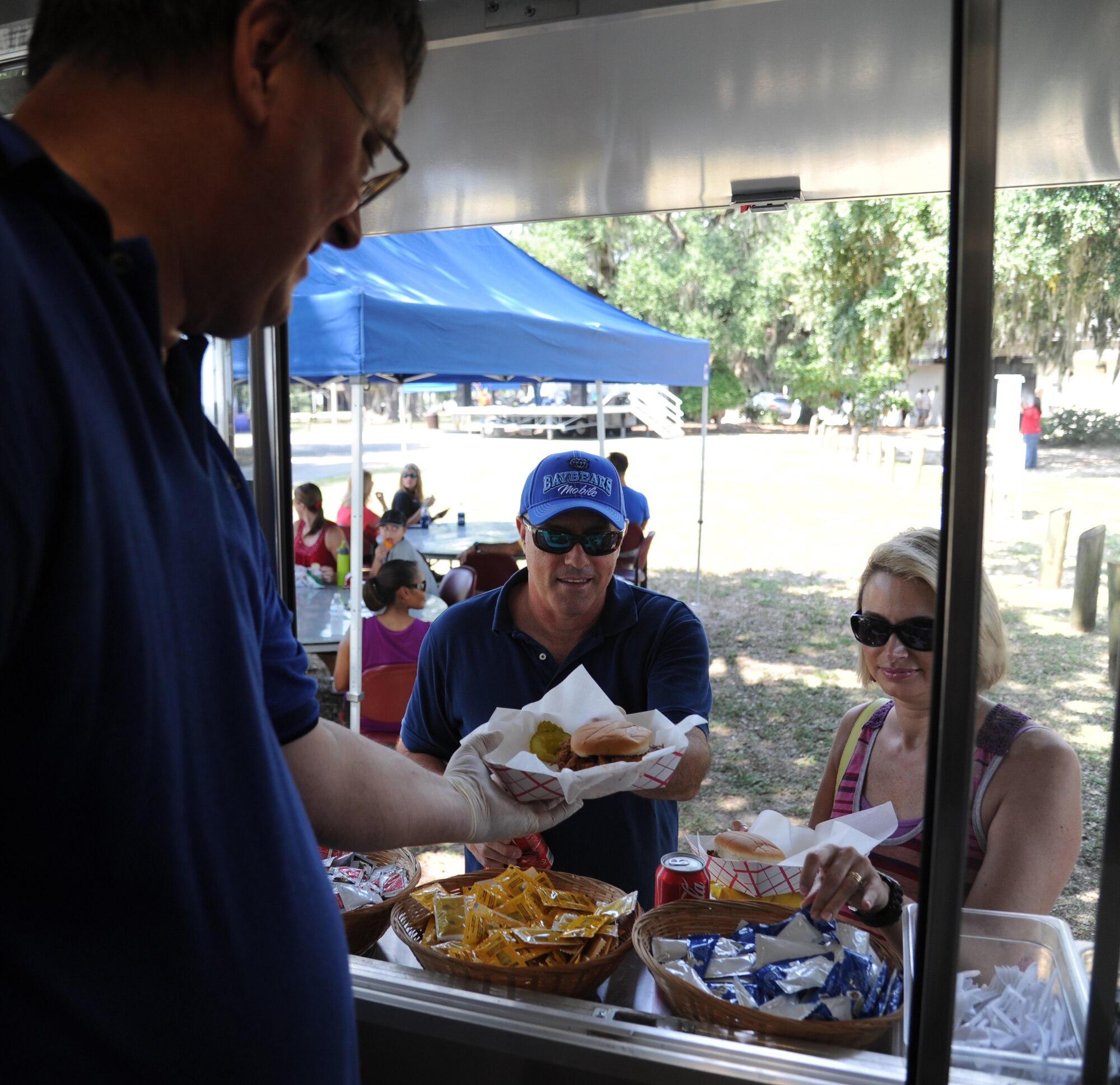 Tom Butler, 81st Force Support Squadron, serves pork sandwiches to Lt. Col. Tommy Gunter, Combat Readiness Training Center, Gulfport, Miss., and his wife, during the BBQ on the Bay event Aug. 23, 2014, at the Marina Park, Keesler Air Force Base, Miss.  Entertainment also included live music and a Mullet toss competition.  (U.S. Air Force photo by Kemberly Groue)
