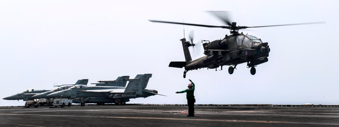 A U.S. sailor guides an Army AH-64 Apache helicopter to the flight deck of the aircraft carrier USS George H.W. Bush during flight operations in the Arabian Gulf, Aug. 18, 2014.