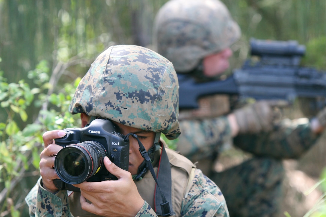 U.S. Marine Corps Lance Cpl. Mark Corpuz, a combat lithographer with Marine Forces Pacific, simulates taking a photo while Marines from the 3rd Battalion, 3rd Marine Regiment simulate patrol techniques during a photo shoot for Marine Corps Systems Command (MARCORSYSCOM) at Marine Corps Base Hawaii March 24, 2010. MARCORSYSCOM requested visual imagery showing the use of Canon camera gear in an operational environment. (U.S. Marine Corps photo by Lance Cpl. Jody Lee Smith/Released)