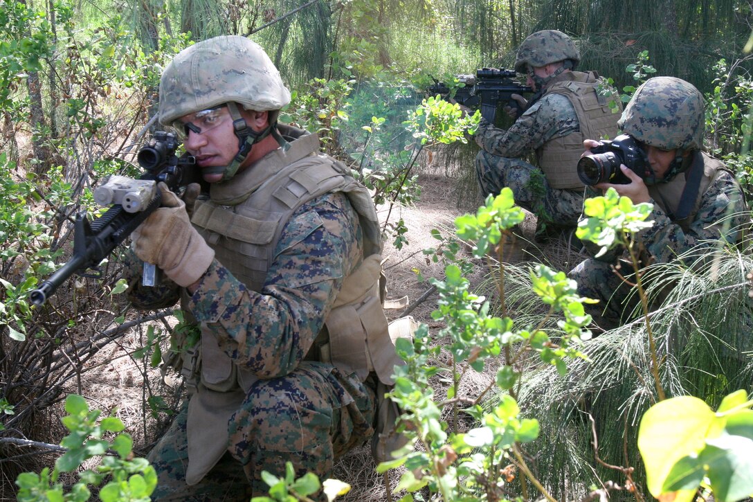 U.S. Marine Corps Lance Cpl. Mark Corpuz, a combat lithographer with Marine Forces Pacific, simulates taking a photo while Marines from the 3rd Battalion, 3rd Marine Regiment simulate patrol techniques during a photo shoot for Marine Corps Systems Command (MARCORSYSCOM) at Marine Corps Base Hawaii March 24, 2010. MARCORSYSCOM requested visual imagery showing the use of Canon camera gear in an operational environment. (U.S. Marine Corps photo by Lance Cpl. Jody Lee Smith/Released)