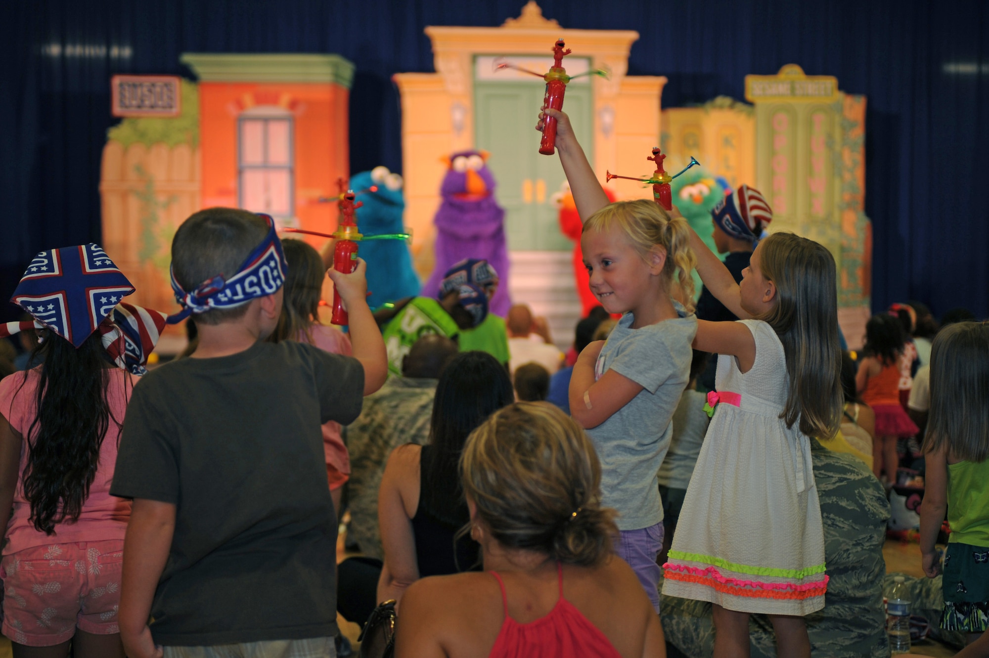Military children hold up their toys during a Sesame Street performance at Davis-Monthan Air Force Base Ariz., Aug 26, 2014. The Sesame Street USO Experience for Military Families is a show that is intended to help children learn new ways to make friends and keep in touch with old ones when they’ve moved to a new installation. (U.S. Air Force photo by Airman 1st Class Cheyenne Morigeau/ Released) 