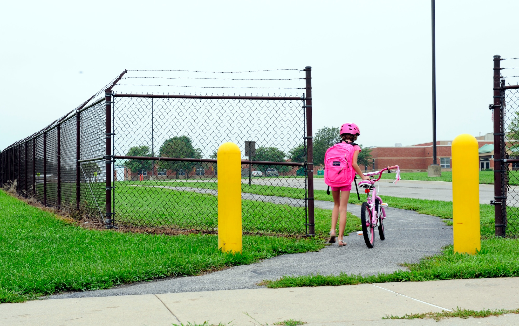 Children use the Patriots Landing housing pedestrian gate to ride their bikes to Scott Elementary School August 18, 2014. Individuals using the gate must walk through it. This requires children who ride bikes to stop and get off then walk ensuring safety because of the large amount of traffic.  (U.S. Air Force photo/Staff Sgt. Stephenie Wade)