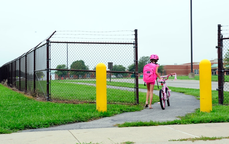 Children use the Patriots Landing housing pedestrian gate to ride their bikes to Scott Elementary School August 18, 2014. Individuals using the gate must walk through it. This requires children who ride bikes to stop and get off then walk ensuring safety because of the large amount of traffic. (U.S. Air Force photo/Staff Sgt. Stephenie Wade)