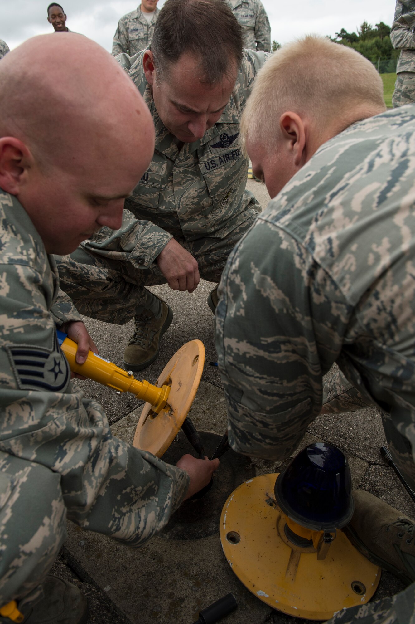 U.S. Air Force Staff Sgt. Matthew Messelheiser, 52nd Civil Engineer Squadron electrical system craftsman, and U.S. Air Force Airman 1st Class Johnathan Fude, 52nd CES electrical engineer, instruct U.S. Air Force Col. Pete Bilodeau, 52nd Fighter Wing commander, how to change a taxiway light, Aug. 26, 2014, at Spangdahlem Air Base, Germany. Spangdahlem is the first base in U.S. Air Forces in Europe and Air Forces Africa to use all Light-Emitting Diode lights for its taxiways.  (U.S. Air Force photo by Staff Sgt. Christopher Ruano/Released)