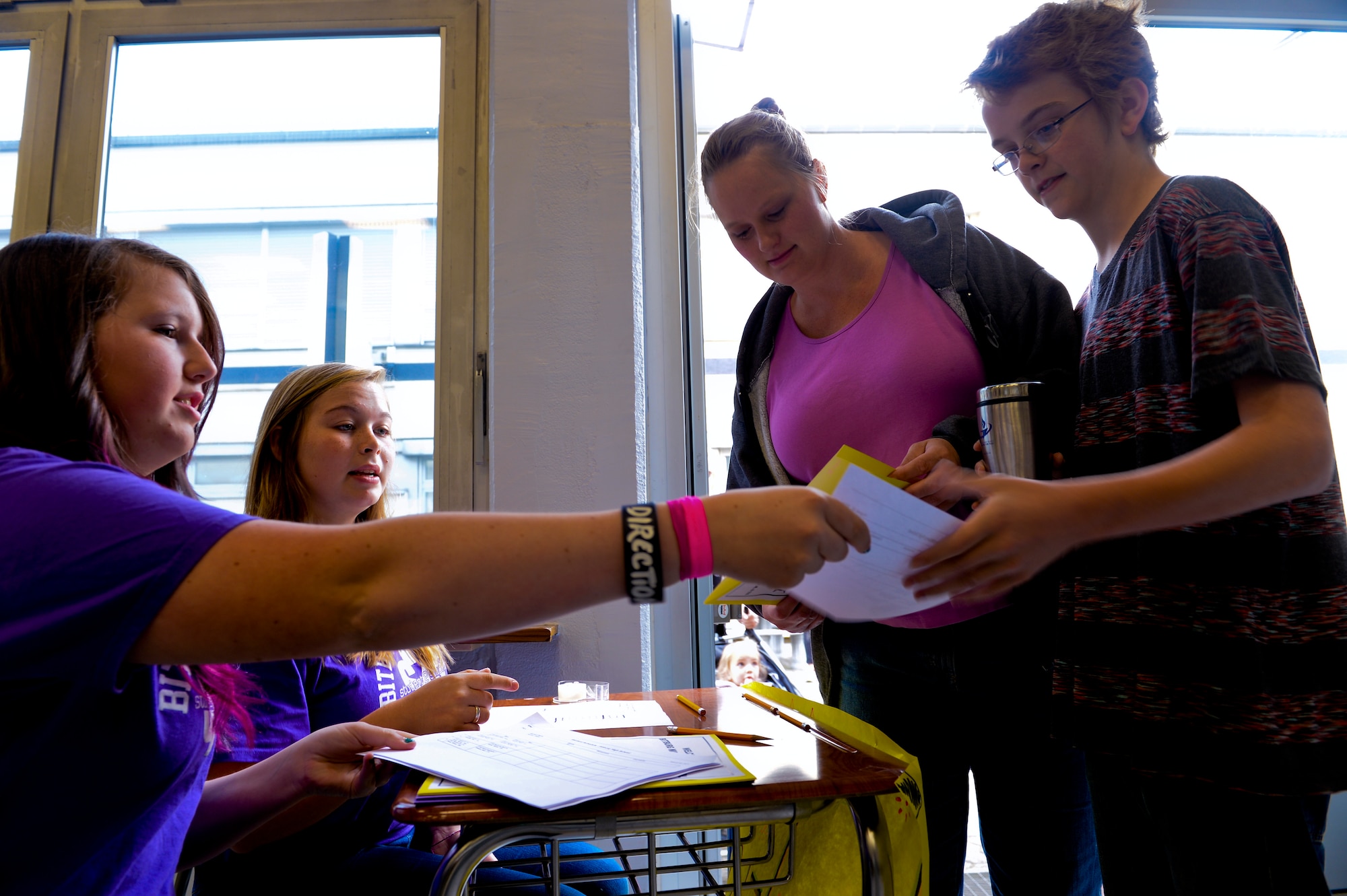 Gavin Lerch, right, a 7th grade student at Bitburg Middle-High School, son of Bernadette and U.S. Air Force Master Sgt. Martin Lerch, 52nd Force Support Squadron first sergeant, takes a student folder from an Student 2 Student member at the school auditorium at Bitburg Annex, Germany, Aug. 22, 2014. Lerch attended the orientation event with his mother, Bernadette, picture left. (U.S. Air Force photo by Airman 1st Class Timothy Kim/Released)