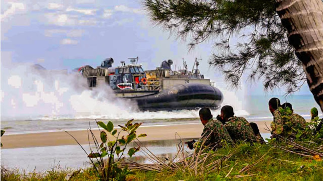 Members of the Malaysian Armed Forces observe as a landing craft air cushion carrying Marines and sailors from the 11th Marine Expeditionary Unit and Amphibious Squadron Five arrives on a beach during Malaysia-United States Amphibious Exercise 2014. MALUS AMPHEX 14 is a bilateral exercise between the 11th MEU and Malaysian Armed Forces that includes operational and tactical level training in planning, command and control, and combat service support using both ground and sea assets. 
