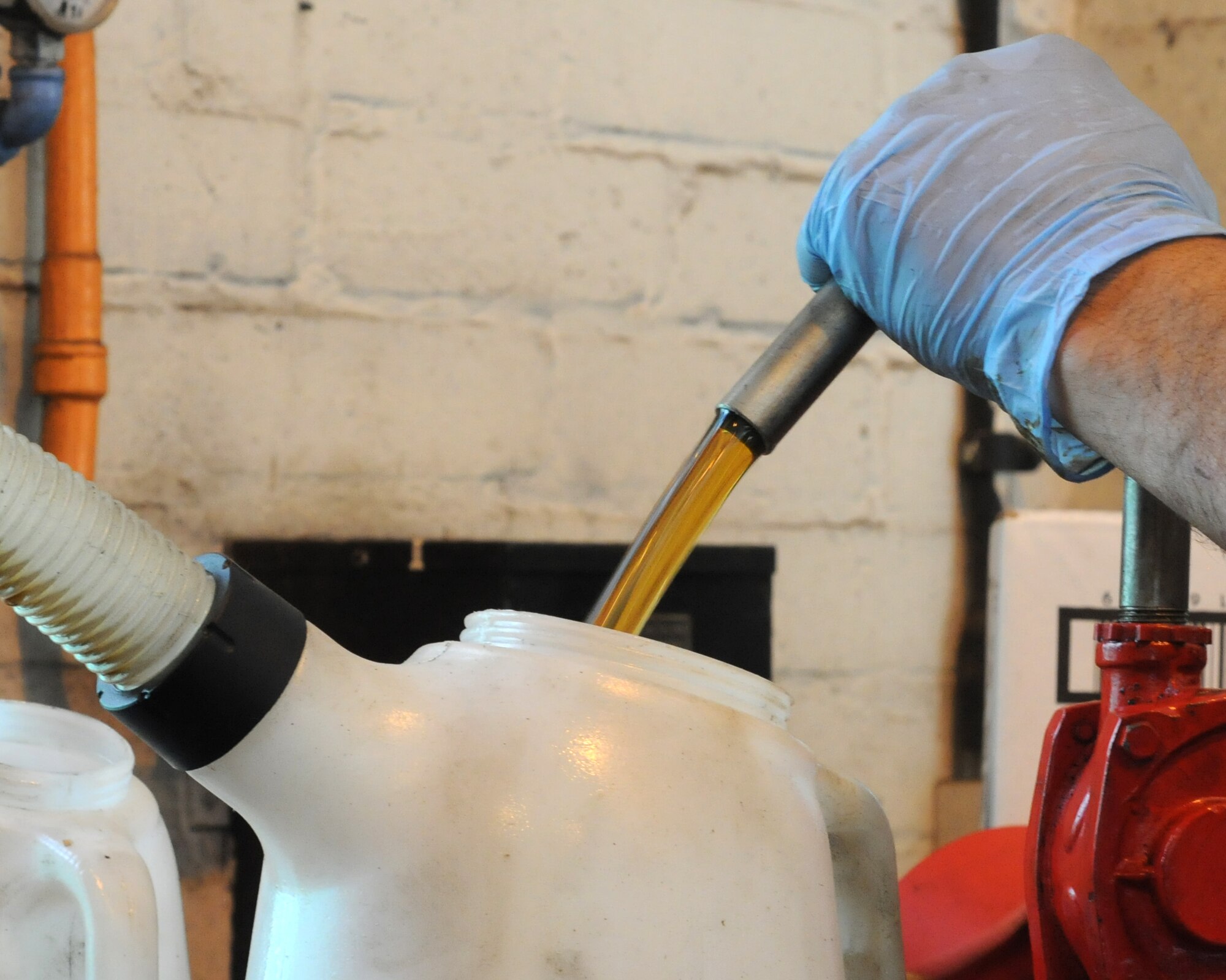 Alejandro Soto, 100th Force Support Squadron auto hobby shop technician from McFarland, Calif., pumps fresh oil into a container so he can funnel it into a vehicle’s oil tank Aug. 13, 2014, at the auto hobby shop on RAF Mildenhall, England. The oil that is used by the auto hobby complex is always the correct grade for the vehicle being serviced. (U.S. Air Force photo/Gina Randall/Released)