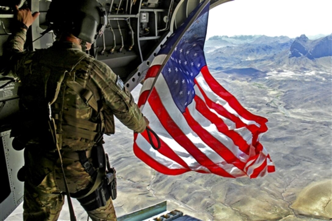 U.S. Army Sgt. Michael Misheff flies the American flag from the back of a CH-47 Chinook helicopter over southern Kandahar province, Afghanistan, Aug. 24, 2014. Misheff is a crew chief assigned to 16th Combat Aviation Brigade. The pilots and crew chiefs fly American flags to present with certificates to service members as part of aviation tradition.