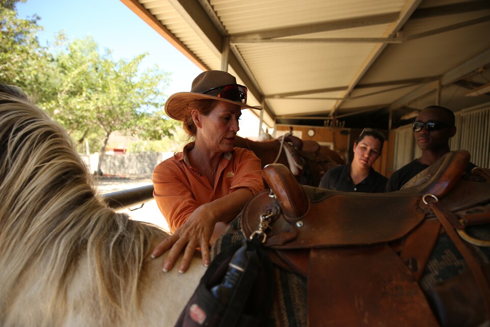 Jacklyn Wilson, owner, Crazy Horse Ranch, conducts a class for Pfc. Sandra Cuellar, administration specialist, Installation Personnel Administration Center, and Cpl. Thomas Salukumbo, administrative specialist, IPAC, during a volunteer event in one of the stables of Crazy Horse Ranch, Aug. 24, 2014. Wilson’s approach to horsemanship focuses on suggestion as opposed to submission.