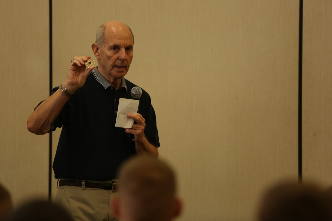 Gene Wuestenfield, president, Phoenix Chapter, 1st Marine Division Association, explains the design of the coin being presented to E Co., 2nd Battalion, 7th Marine Regiment, during a coin presentation ceremony, at Building 1707 aboard the Combat Center, Aug. 22, 2014. The coin presentation and Oscar P. Austin award has been presented to Co. E, 2/7 annually for the past 20 years.