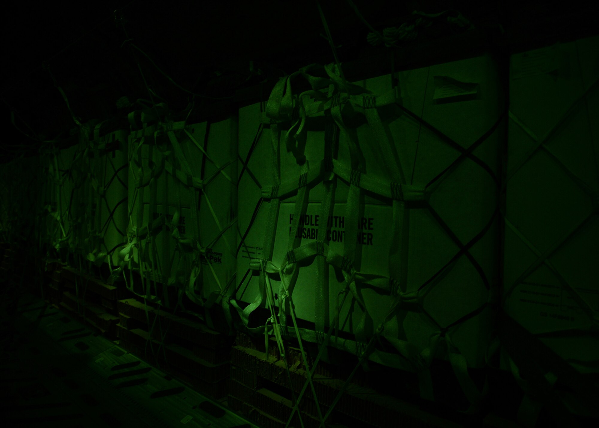 Container delivery system bundles filled with fresh drinking water sit in the dark on C-17 Globemaster III in preparation for a humanitarian airdrop over the area if Amirli, Iraq Aug. 31, 2014. Lights are dimmed or shut off completely to lower visibility to threats from the ground. The airdrop included two C-17s and two C-130 Hercules delivering 10,545 gallons of fresh drinking water and 7,056 Halal Meals Ready to Eat. (U.S. Air Force photo by Staff Sgt. Shawn Nickel)