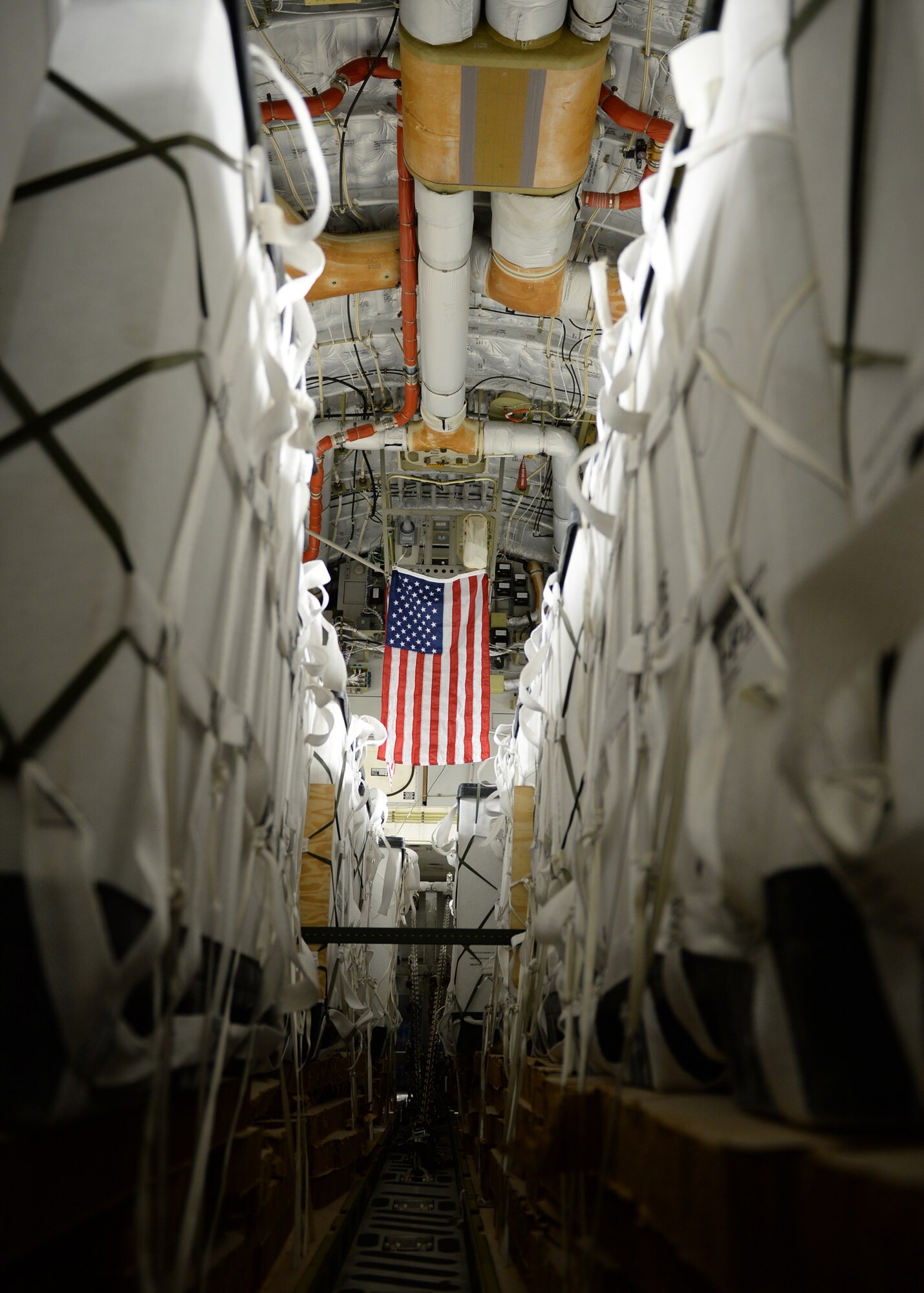 An American flag hangs above 40 container delivery system bundles filled with fresh drinking water on a C-17 Globemaster III for a humanitarian airdrop over the area if Amirli, Iraq Aug. 30, 2014. Two C-17s and two C-130 Hercules dropped 10,545 gallons of water and 7,056 Halal Meals Ready to Eat. (U.S. Air Force photo by Staff Sgt. Shawn Nickel)