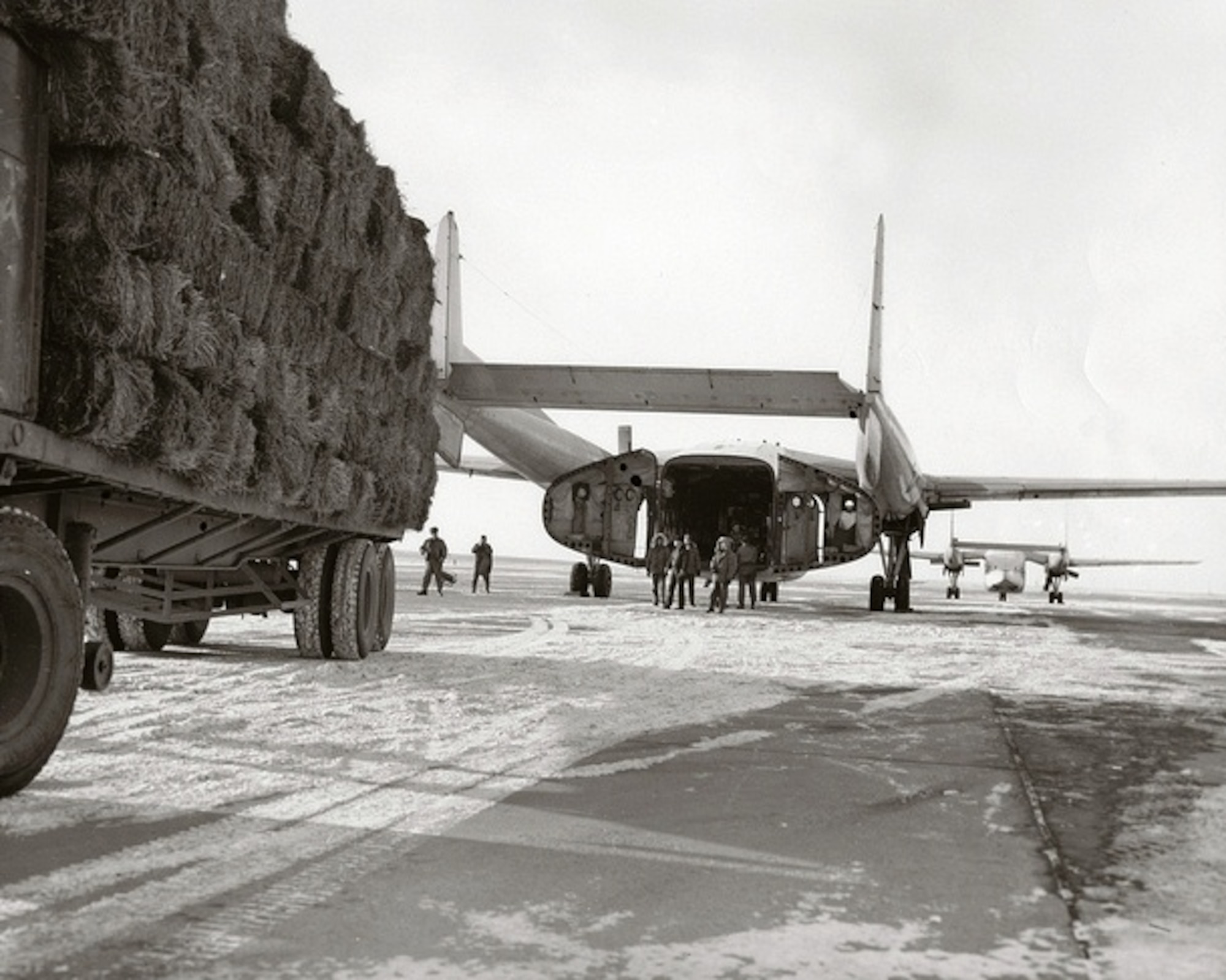 Airmen load hay onto a C-119 Flying Boxcar in December of 1964 on the runway at Malmstrom Air Force Base, Mont. Frigid temperatures and heavy snowfall during the month of December led to the declaration of a major disaster for southwest Montana. Ranchers suffered major livestock losses resulting from extreme negative temperatures and snowfall, and landowners were unable to reach their cattle and sheep.  Cargo aircraft from five reserve units were mobilized to help drop hay to the stranded animals. The Air Reserve units managed to drop 65 tons of hay to about 100,000 head of livestock during Operation Hay Lift, using low-level drops of hay bales to the stranded animals. (Courtesy photo)