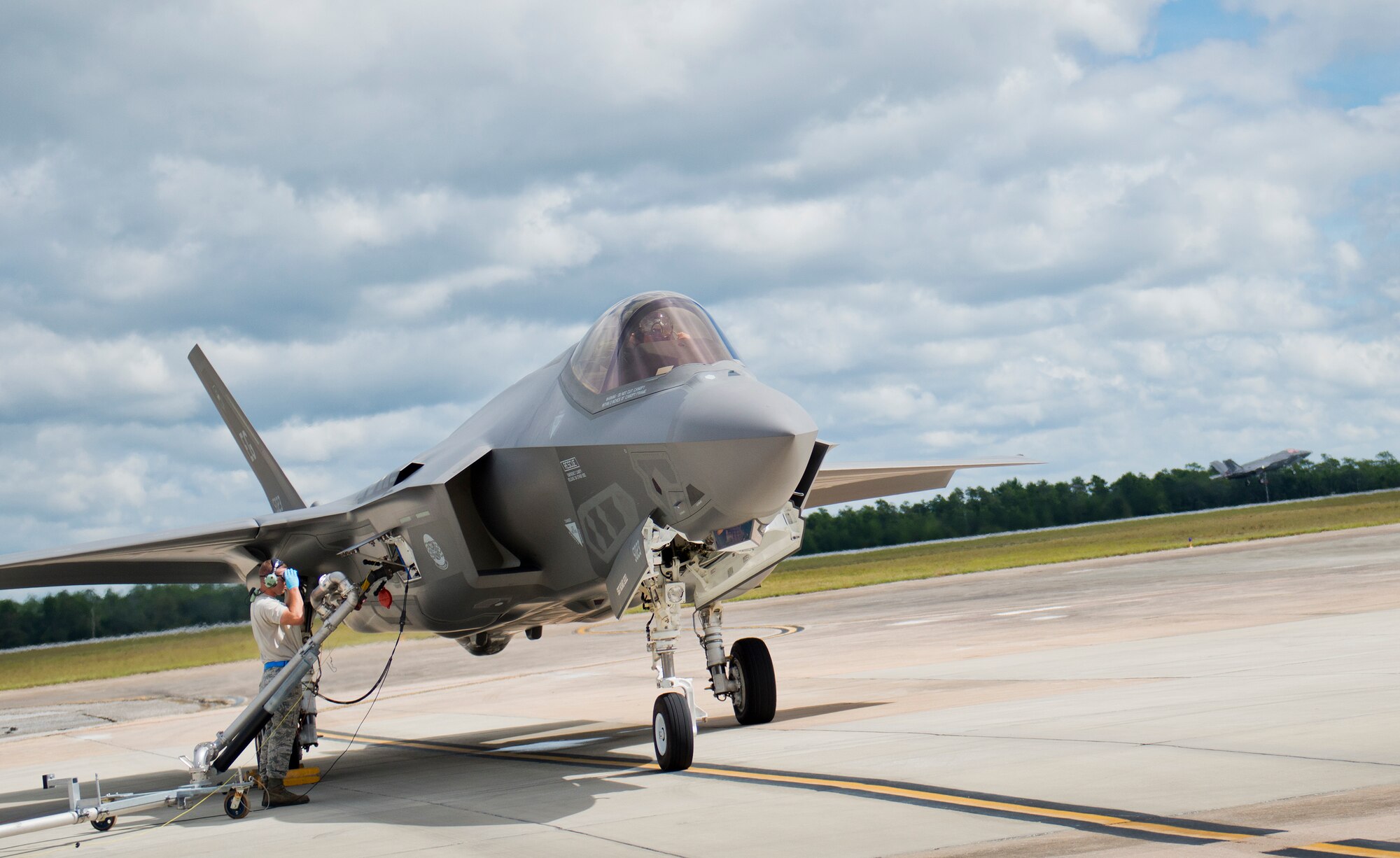Staff Sgt. Chris Hunter, 33rd Aircraft Maintenance Squadron, connects the gas pump to an F-35A Lightning II as another joint strike fighter lifts off the Eglin Air Force Base runway.  All of the F-35 variants use the refueling areas in conjunction with the 96th Logistics Readiness Squadron’s fuels flight. (U.S. Air Force photo/Samuel King Jr.)  