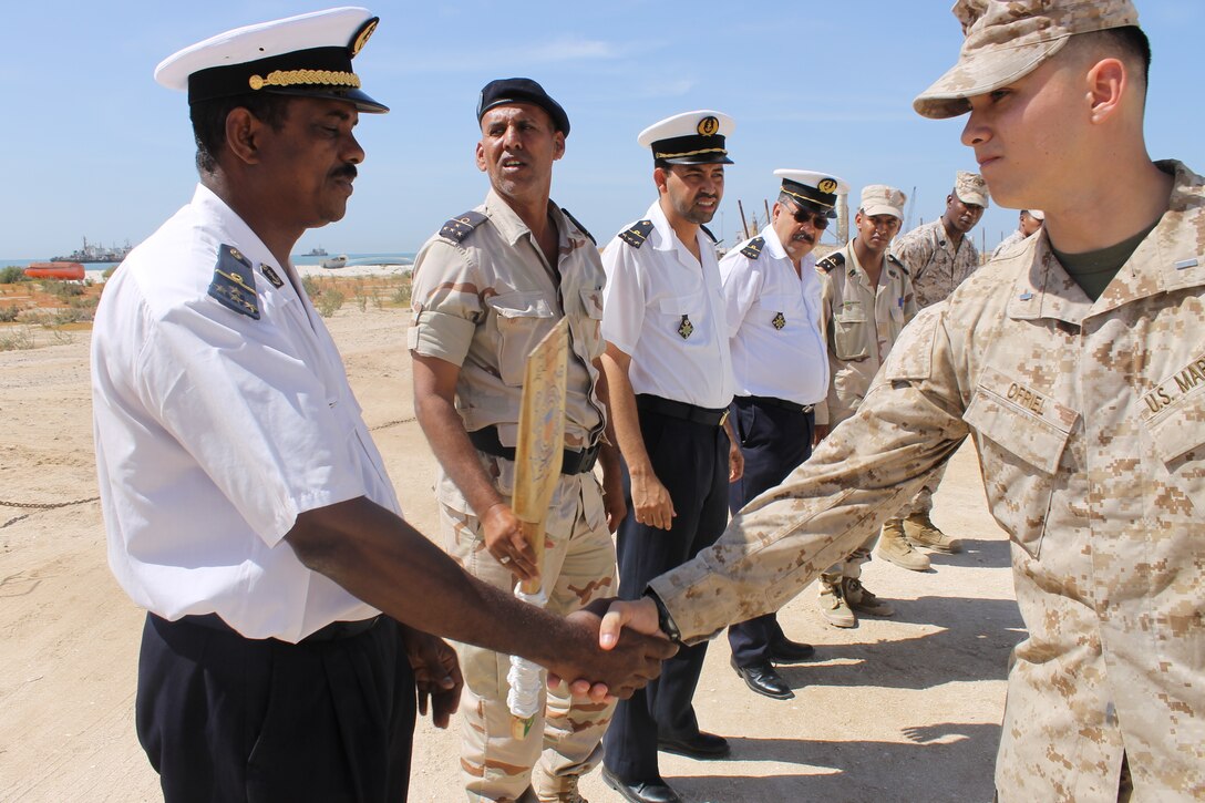 1st Lieutenant Michael O’Friel (right) shakes hands with a Naval Officer from the La Marine Nationale Mauritanienne (Mauritanian Navy) in Mauritania, Nov. 13, 2014. O’Friel is the officer-in-charge of Security Cooperation Team-7, a group of Marines and Coast Guardsmen from SPMAGTF-Crisis Response-Africa working alongside the Mauritanian Navy, teaching outboard motor maintenance.(Courtesy Photo by Petty Officer 2nd Class Michael Vadala, U.S. Coast Guard)