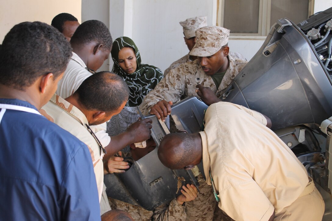 Machinery Technician Third Class Janneh Felix (right center) assists service members with the La Marine Nationale Mauritanienne (Mauritanian Navy) in reinstalling the lower unit of an outboard motor. Felix is a Coast Guardsmen with SPMAGTF-Crisis Response-Africa who was deployed to Mauritania to conduct an outboard motor maintenance course with service members from the La Marine Nationale Mauritanienne, Nov. 13, 2014. (Courtesy Photo by Petty Officer 2nd Class Michael Vadala, U.S. Coast Guard)
