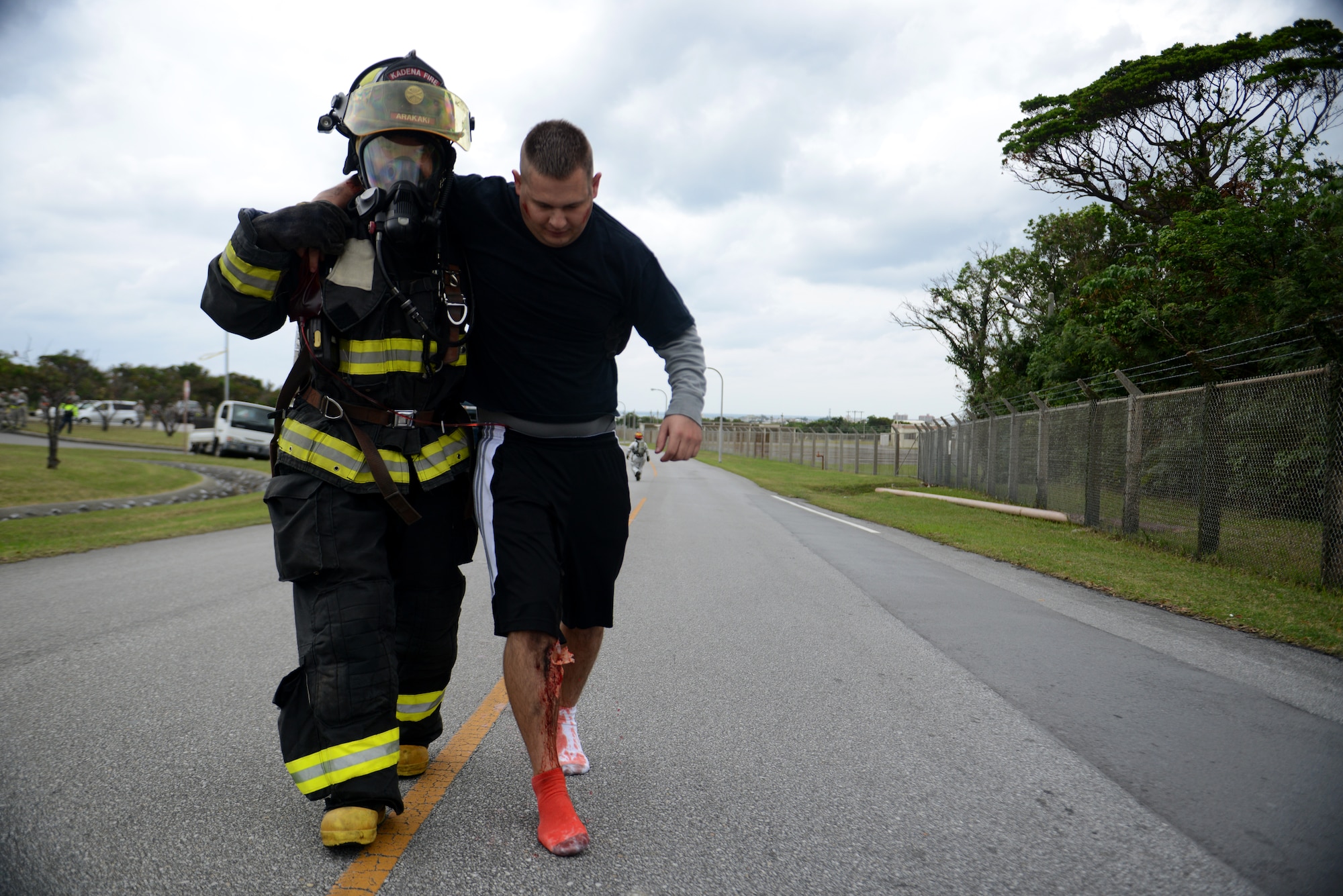 A firefighter from the 18th Civil Engineer Squadron assists a victim of a simulated hazardous materials vehicle crash as part of a mission focused exercise on Kadena Air Base, Japan, Dec. 2, 2014. During MFEs, wing inspection team members use special makeup on simulated casualties to provide realism to the different training scenarios. (U.S. Air Force photo by Senior Airman Maeson L. Elleman/Released) 