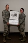 Col. Kevin Kennedy, 28th Bomb Wing Commander, presents Airman 1st Class Mackenzie Alderson, 28th Munitions Squadron line delivery crewmember, the winning foreign object debris poster of the year at Ellsworth Air Force Base, S.D. Nov. 20, 2014. Each month, Airmen compete against each other for the best FOD poster design, winners are then selected to compete for the FOD poster of the year. (U.S. Air Force photo by Airman 1st Class Rebecca Imwalle/Released)