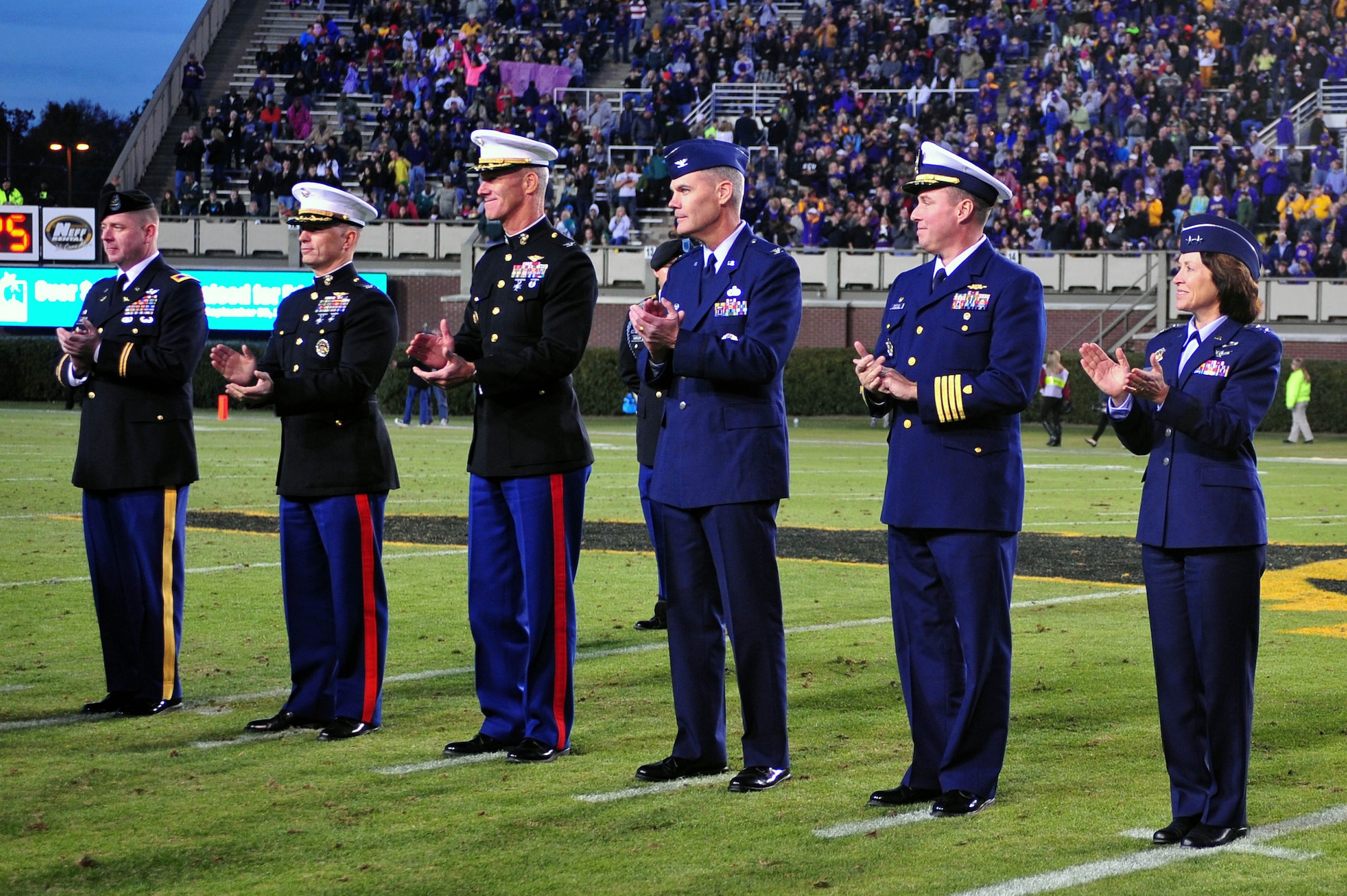 Service members join in applause during East Carolina University’s military appreciation day at Dowdy-Ficklen Stadium in Greenville, North Carolina, Nov. 22, 2014. The ECU Pirates hosted the Tulane University Green Wave, winning the game 34-6. Dr. Steve Ballard, East Carolina University chancellor, presented a coin to Col. Darrell Steele (third from right), 4th Maintenance Group commander, during the halftime ceremony. Ballard offered a commemorative coin in appreciation for those serving in the armed forces. (U.S. Air Force photo/Senior Airman John Nieves Camacho)