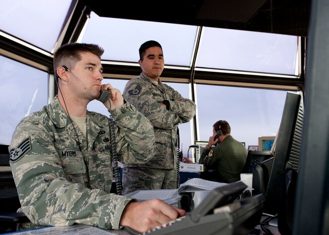 Staff Sgt. Arturo Herrera (right), 57th Operations Support Squadron tower watch supervisor, observes Staff Sgt. Chris Myers, 57th OSS tower air traffic controller, in the control tower at Nellis Air Force Base, Nev., Dec. 2, 2014. The control tower is in charge of and responsible for managing the air space over Nellis AFB. (U.S. Air Force photo by Senior Airman Thomas Spangler)